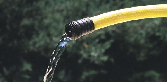 Close-up of water pouring from the nozzle of a bright yellow garden hose, with a blurred green background.